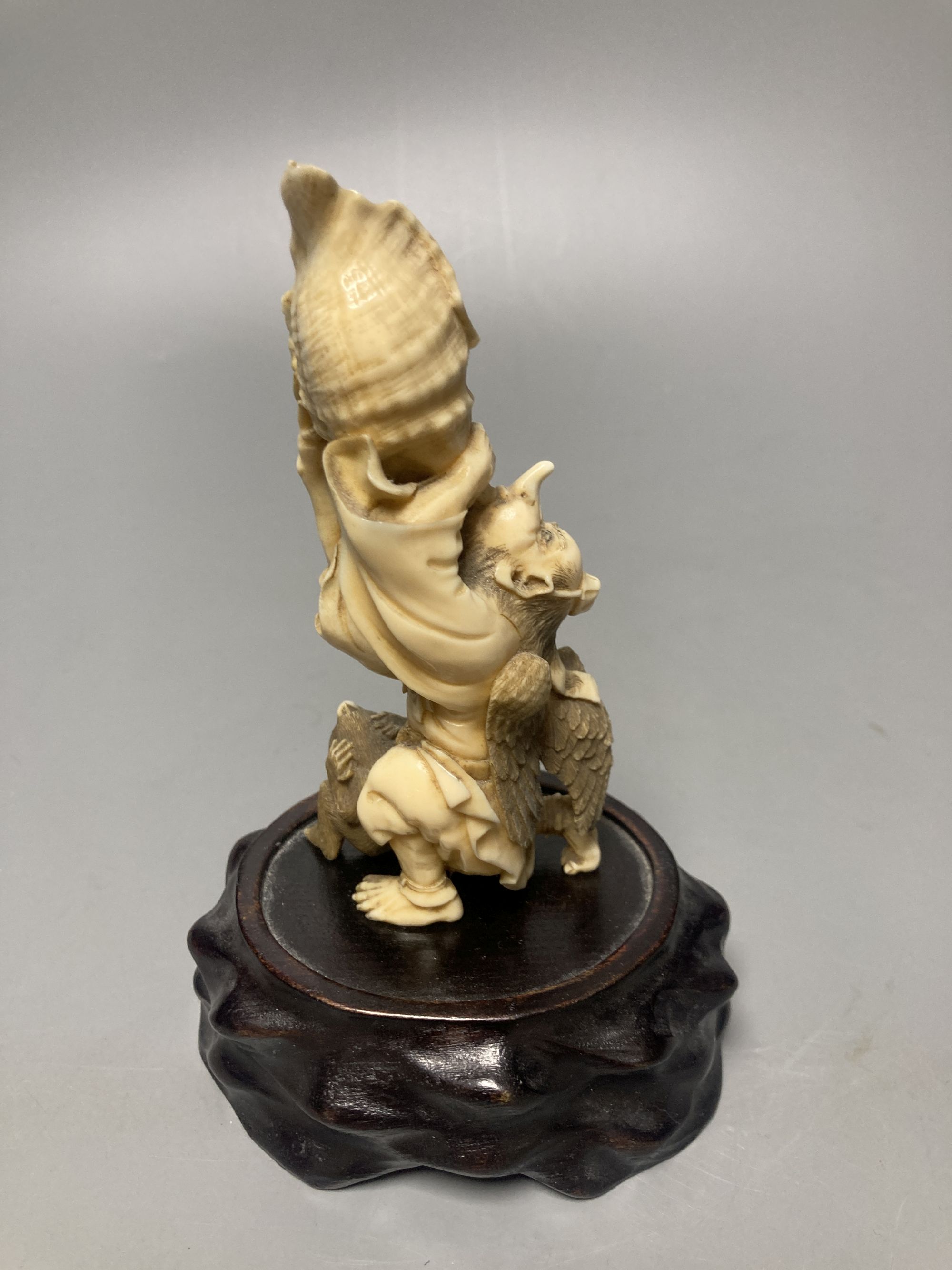 A Japanese ivory okimono of a winged man blowing a conch, monkey below, Meiji, 89 grams